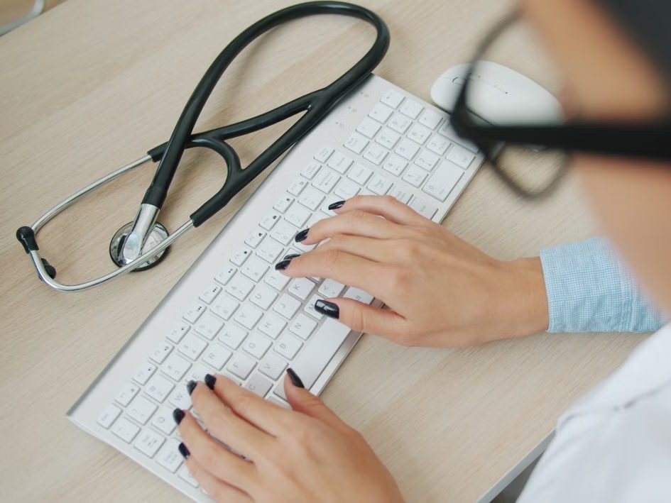 Profesional sanitaria escribiendo en el ordenador, con el fonendoscopio sobre la mesa